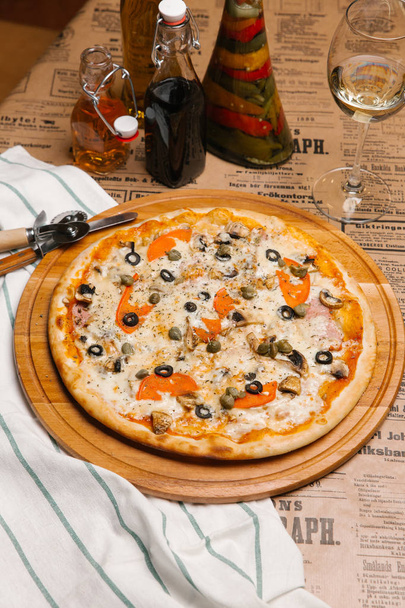 Pizza de queijo com presunto, cogumelos, tomates, azeitonas e alcaparras
 - Foto, Imagem