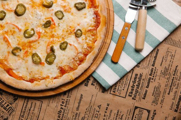 Pizza de queso con jalapeño servida en bandeja de madera y servilleta rayada
 - Foto, imagen