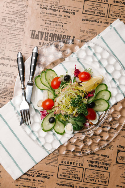 Овощной салат с огурцами, луком-порей, оливками, тунцом и перепелиными яйцами подается на хрустальной пластине
 - Фото, изображение