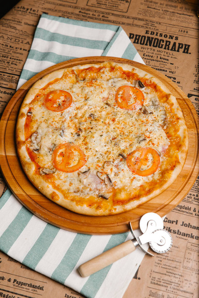 Pizza al formaggio con pomodori, prosciutto e funghi servita su vassoio di legno
 - Foto, immagini