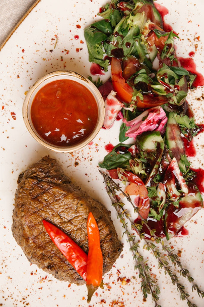 rib eye steak met salade en tomaat saus op witte plaat - Foto, afbeelding