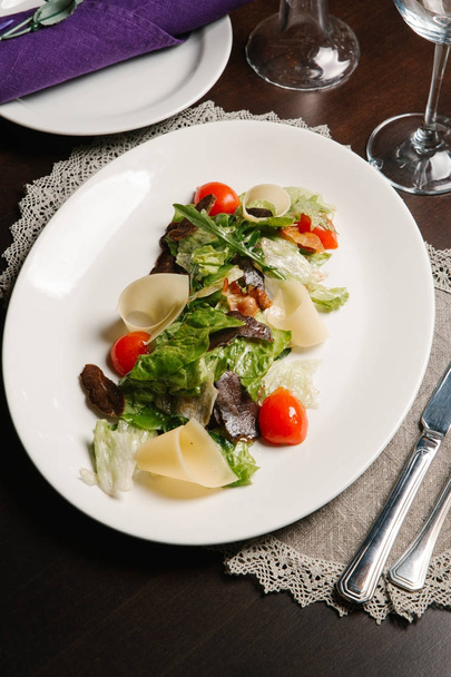 Вид зверху на салат з руколою, яловичиною, вишневими помідорами та сиром, поданий на білій тарілці з столовими приборами та серветкою
 - Фото, зображення