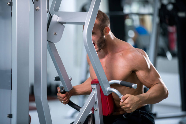 Determinado jovem homem muscular trabalhando na máquina de fitness no ginásio
 - Foto, Imagem