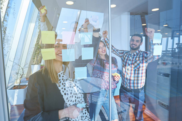 business, startup, planning, management and people concept - happy creative team writing on stickers at office glass board in modern office - Foto, Imagen