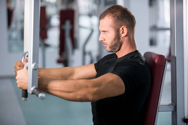 Determined young muscular man working on fitness machine at the gym - Photo, Image
