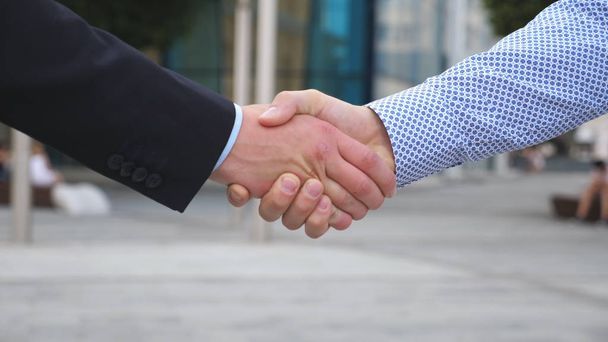 Koledzy spotkać i uścisnąć dłoń w tle miasta. Dwóch biznesmenów witali się w środowisku miejskim. Business handshake odkryty. Potrząsanie męskich ramion poza. Slow motion z bliska - Zdjęcie, obraz