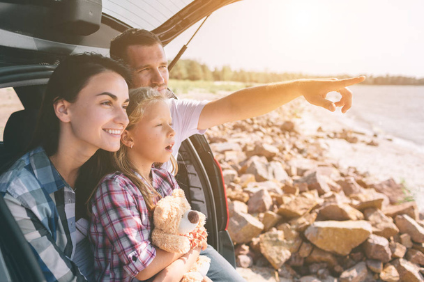 Happy family on a road trip in their car. Dad, mom and daughter are traveling by the sea or the ocean or the river. Summer ride by automobile - Photo, Image