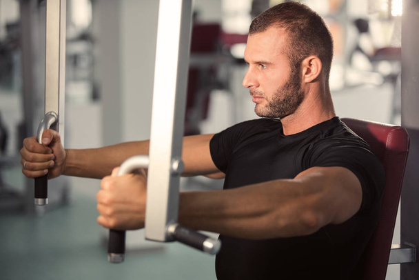 Determined young muscular man working on fitness machine at the gym - Foto, Imagem