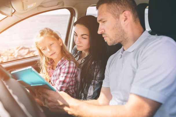 Happy family on a road trip in their car. Dad, mom and daughter are traveling by the sea or the ocean or the river. Summer ride by automobile - Foto, imagen