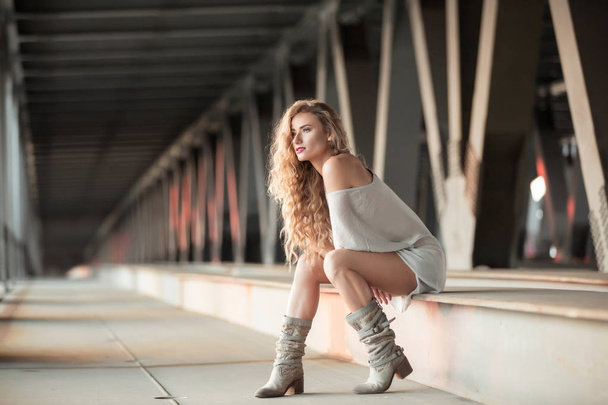 Krásné kudrnaté mladá žena sedící na pohodovou atmosféru průmyslových most - Fotografie, Obrázek