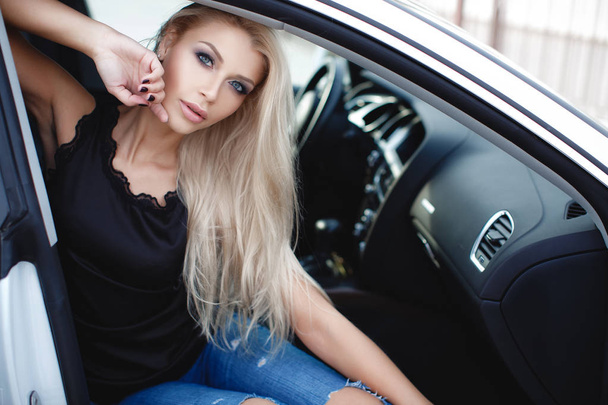Young woman driving a car in the city.Successful, attractive, beautiful, young woman - blonde, sitting at the wheel of an expensive car. Portrait of a beautiful woman in a car looking out of the window and smiling. Travel and vacations concepts - Φωτογραφία, εικόνα