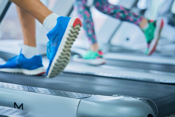 Female muscular feet in sneakers running on the treadmill at the gym - Photo, image