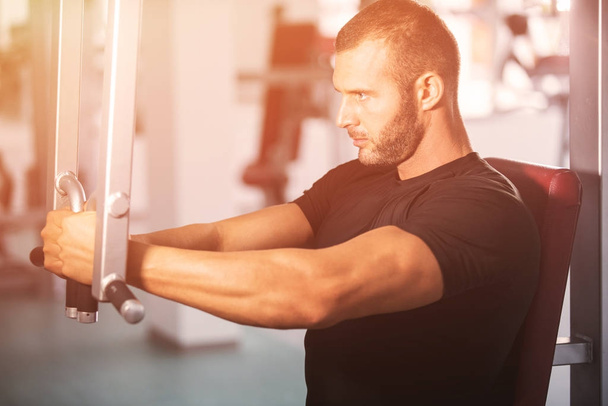 Determined young muscular man working on fitness machine at the gym - Foto, imagen