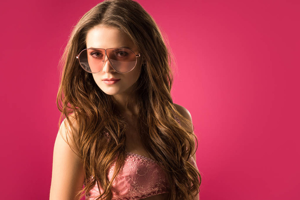 portrait of attractive girl in sunglasses and bra looking at camera isolated on pink  - Фото, зображення