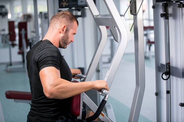 Determined young muscular man working on fitness machine at the gym - Foto, Imagen