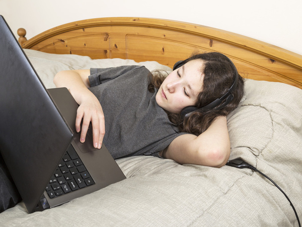 Молода дівчина розслабилася в ліжку на своєму комп'ютері
 - Фото, зображення
