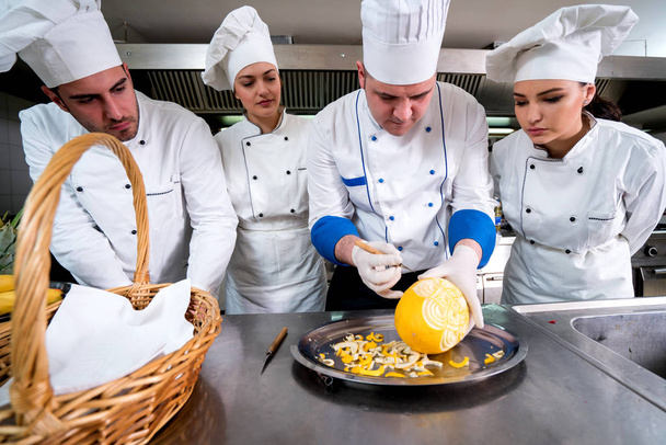 Kitchen chef with young apprentices, teaching to make decorative fruit basket - Foto, Bild