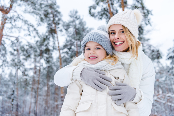muotokuva hymyilevä äiti halaus tytär seistessään talvipuistossa
 - Valokuva, kuva