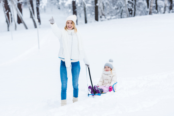 happy daughter and mother sledging together in winter park - Foto, Imagem