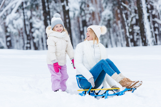 happy daughter and mother sledging together in winter park - Foto, Imagen