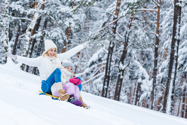 happy daughter and mother sledging together in winter park - Photo, Image