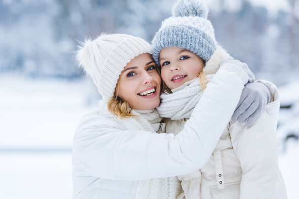 beautiful happy mother and daughter hugging and smiling at camera in winter park - Foto, afbeelding