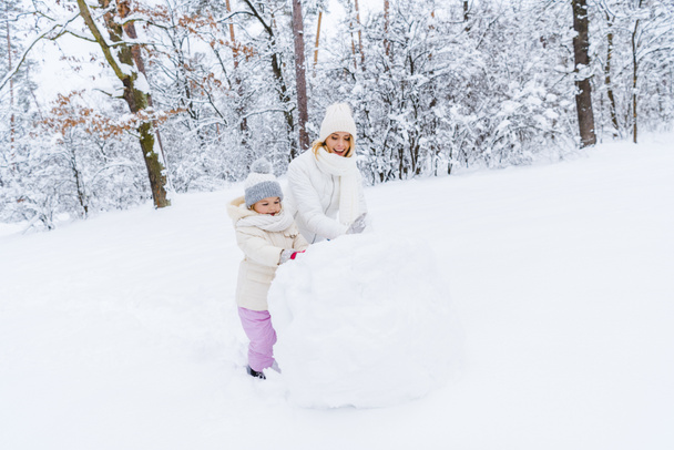 beautiful happy mother and daughter making snowman in winter park - Photo, Image