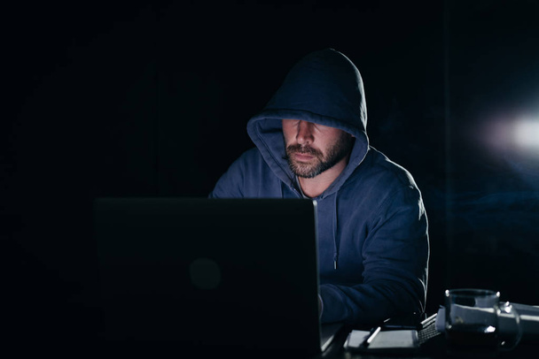 criminal mysterious man doing something illegal on a laptop, in the dark, a hacker - Foto, Bild
