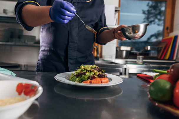 обрізаний знімок шеф-кухаря, який наливає соус на салат
 - Фото, зображення