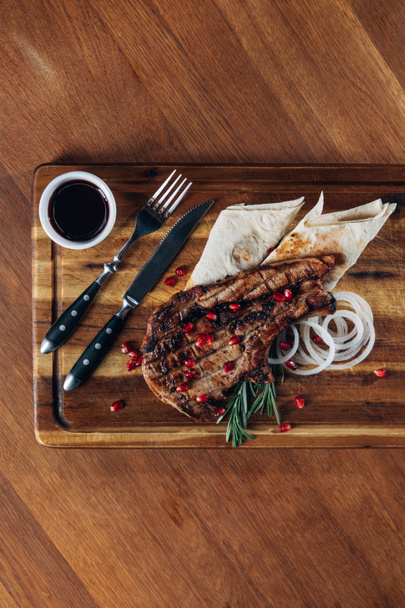 top view of delicious grilled steak served with sauce and pomegranate seeds on wooden board - Foto, afbeelding