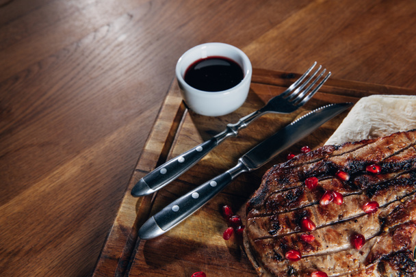 tasty grilled steak served with sauce and pomegranate seeds on wooden board - Photo, Image