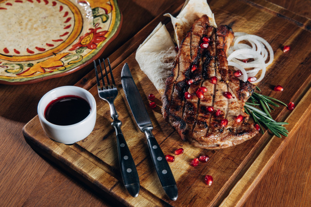 Close-up shot van gegrilde steak geserveerd met saus en de granaatappel zaden op houten bord - Foto, afbeelding