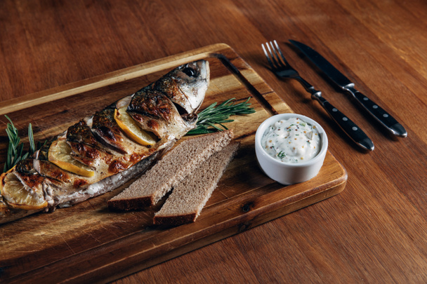 close-up shot of grilled fish with lemon and sauce on wooden board - Photo, Image