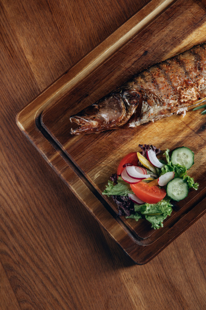 top view of grilled fish with salad on wooden board - Photo, Image
