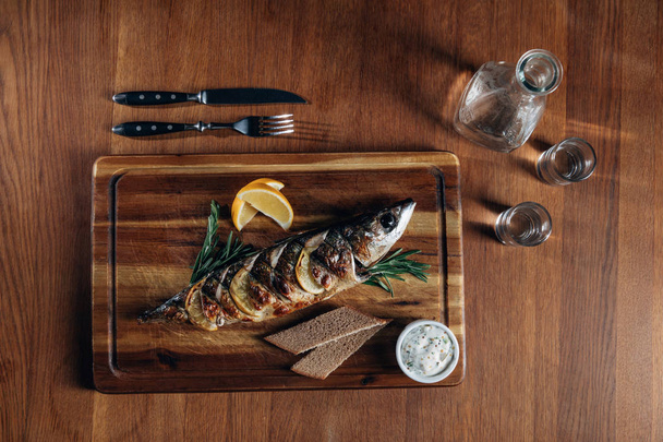 Limonlu ızgara balık üstten görünüm sürahi ve çekim votka ile ahşap tahta üzerinde - Fotoğraf, Görsel