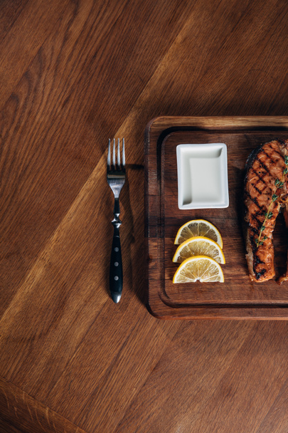 top view of grilled salmon steak served on wooden board with lemon slices - Fotoğraf, Görsel