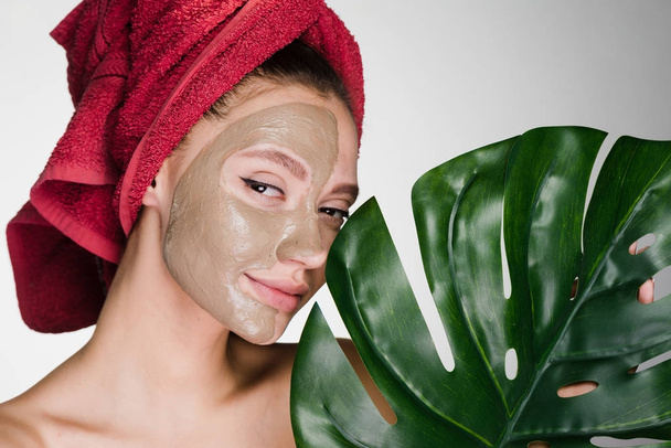 a young smiling girl with a red towel on her head applied a clay mask - Foto, Imagen
