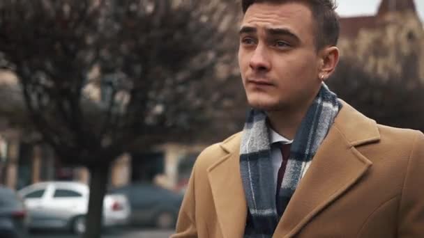 a young businessman in a cloak walking down the street in a cloudy weather. A man goes on the street and dresses. Slow motion - Materiał filmowy, wideo