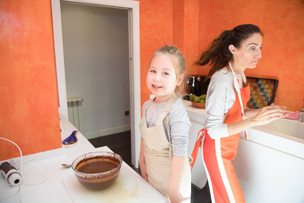 menina olhando e mãe cozinhar um bolo na cozinha
 - Foto, Imagem