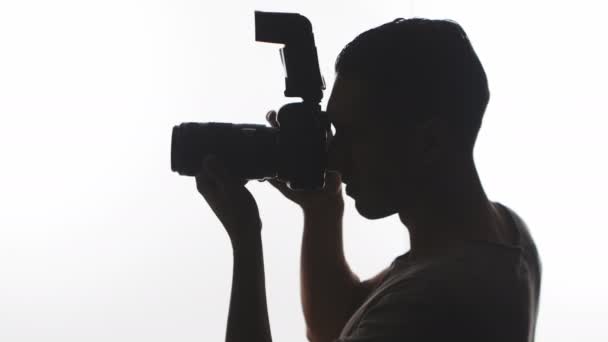 Fotograaf silhouet close-up. Jonge man neemt foto's met Dslr camera geïsoleerd op witte achtergrond - Video