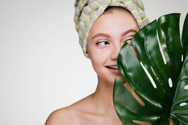 cute smiling girl with a towel on her head holding a green leaf, spa day - 写真・画像