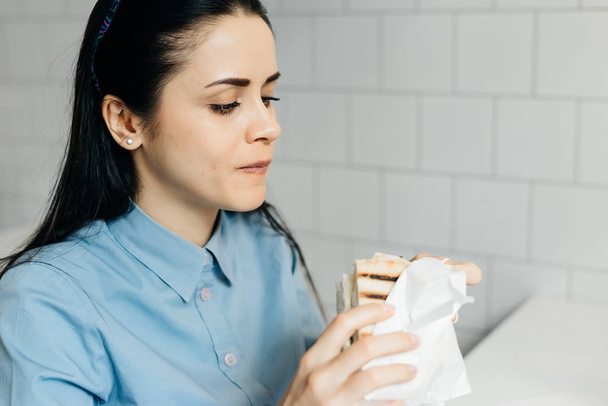 hungry young girl in a blue shirt having a sandwich at a cafe - Foto, Bild