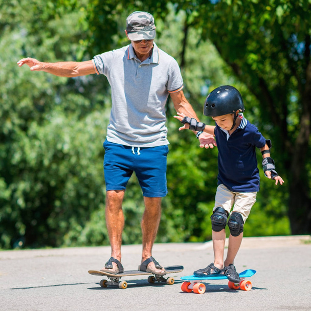 Senior man with little boy skateboarding in park - Photo, Image