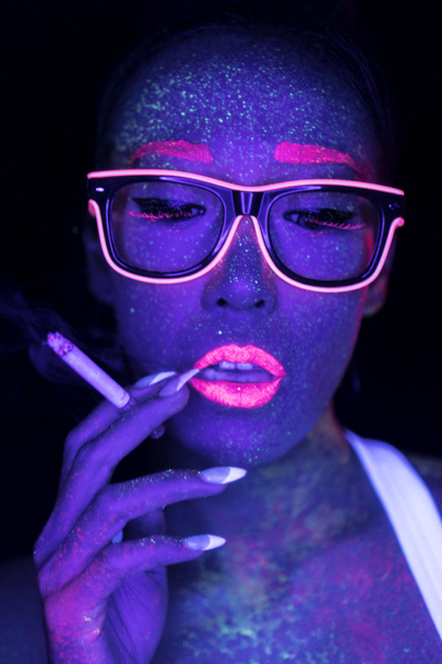 Closeup cara de mulher com fluorescente compõem fumar cigarro, maquiagem criativa olhar grande para discotecas. Festa de Halloween, shows e conceito de música
 - Foto, Imagem
