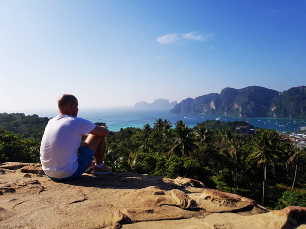 Силуетний чоловік сидить на вершині гори над блакитним морем і фоном неба
 - Фото, зображення
