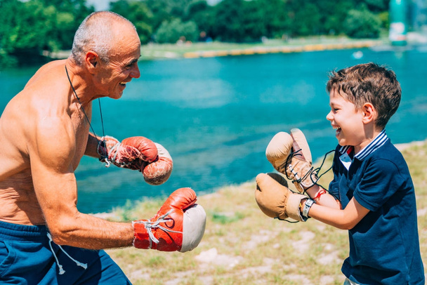 Niño practicando boxeo con abuelo junto al lago
 - Foto, imagen