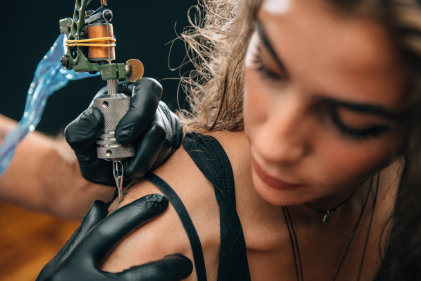  Una chica bonita haciéndose un tatuaje en el hombro. Céntrate en la máquina de tatuaje. Imagen tonificada
 - Foto, Imagen