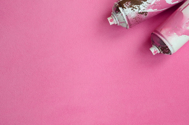Algumas latas de spray de aerossol rosa usadas com gotas de tinta estão em um cobertor de tecido de lã rosa claro macio e peludo. Cor de design feminino clássico. Conceito de hooliganismo de grafite
 - Foto, Imagem