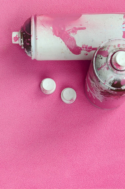 Néhány használt rózsaszín aeroszol spray konzervdobozok és fúvókák festék csöpög fekszik egy takaró puha és Szőrős világos rózsaszín polár anyagból készült. Klasszikus női design színe. Graffiti a huliganizmus koncepció - Fotó, kép