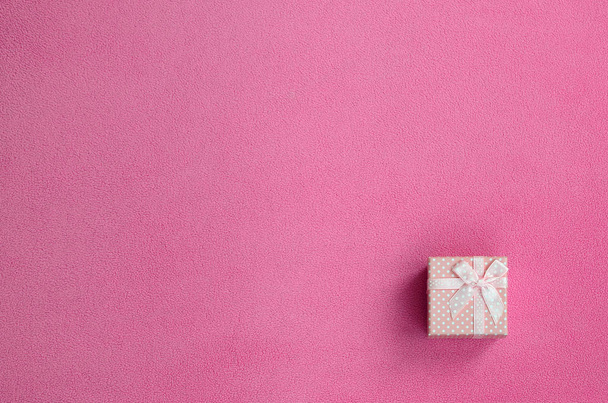 Una pequeña caja de regalo en rosa con un pequeño lazo se encuentra sobre una manta de suave y peludo tejido de lana rosa claro. Embalaje para un regalo a su novia encantadora
 - Foto, imagen